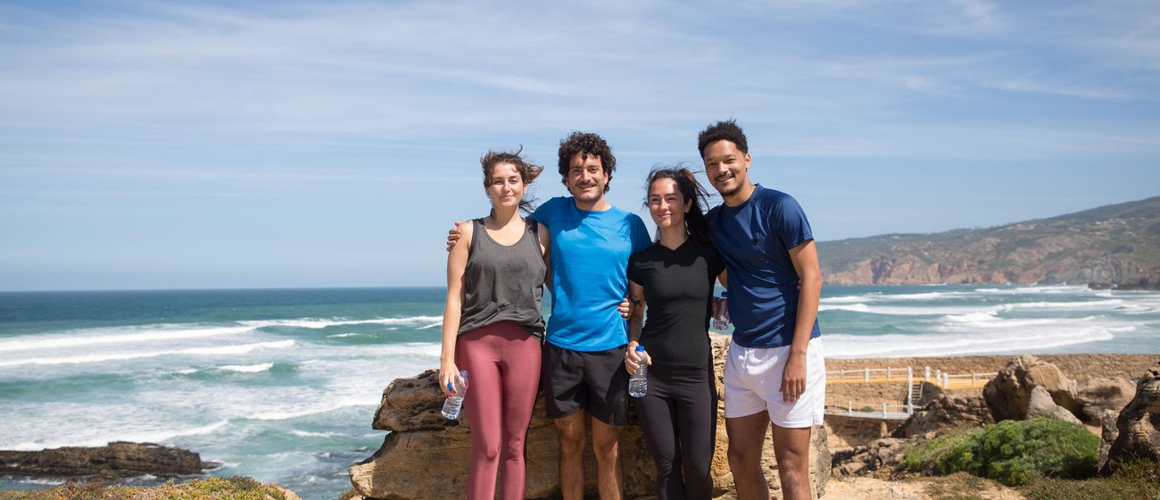 main-kampus-coast Group of four people smiling on a rocky beach overlooking the ocean